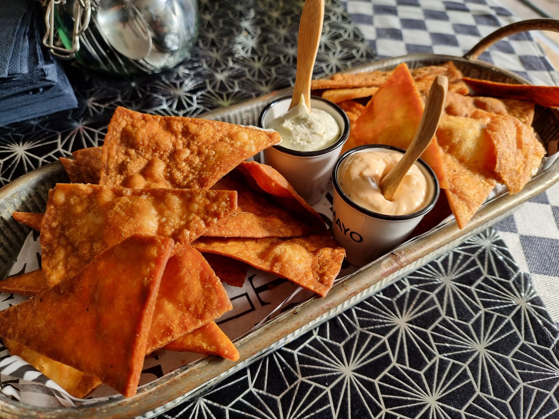 Knapperige gefrituurde tortillachips met twee dipsauzen in kleine witte bakjes, op een metalen dienblad.