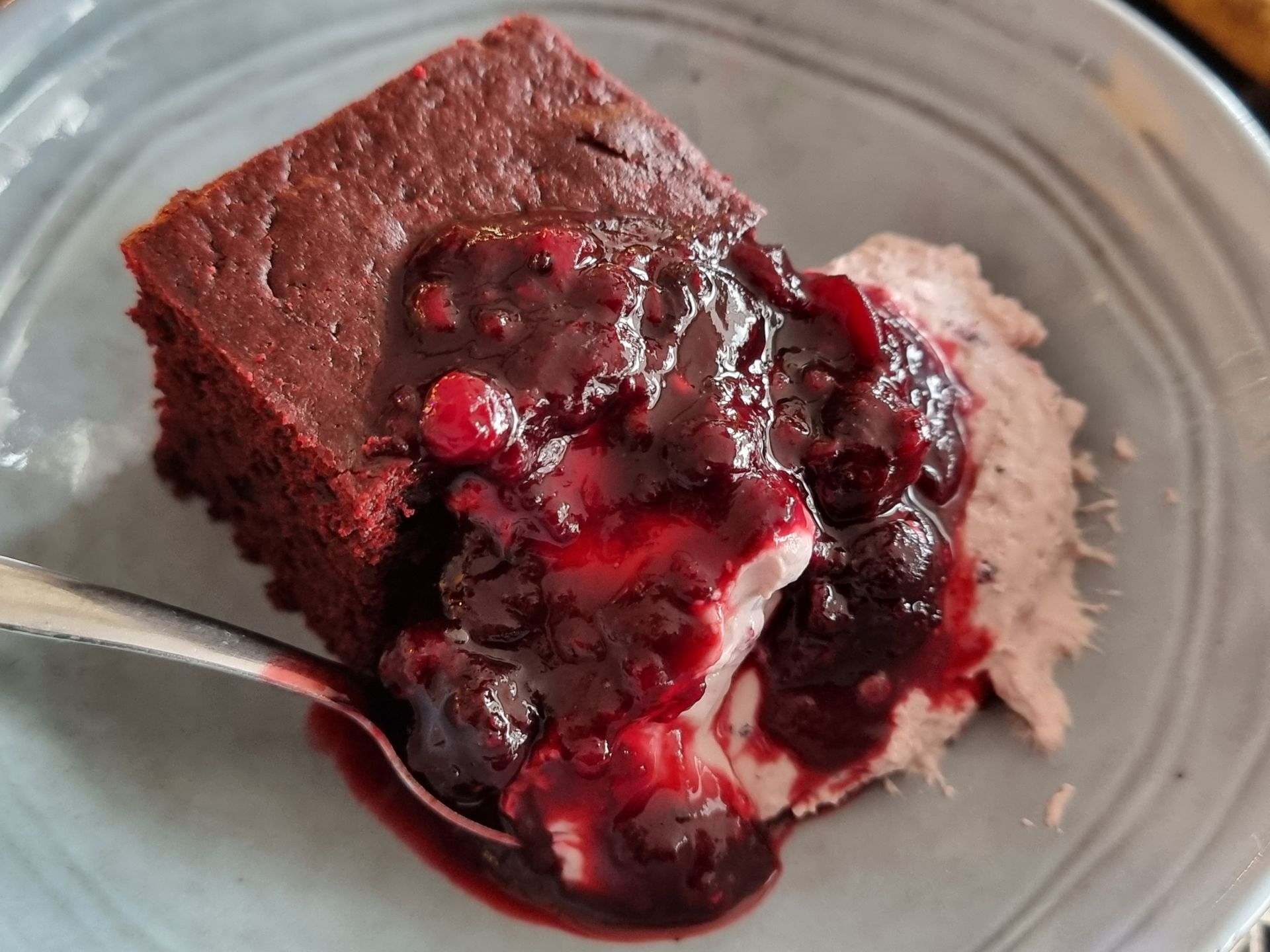 Brownie met rodebessencompote en slagroom, geserveerd op een bord met een lepel.