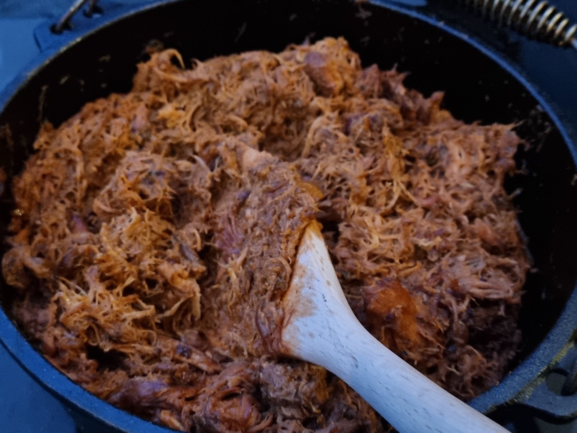 Gesneden, in saus gemarineerd pulled chicken in een braadpan, dat met een houten lepel wordt geroerd.