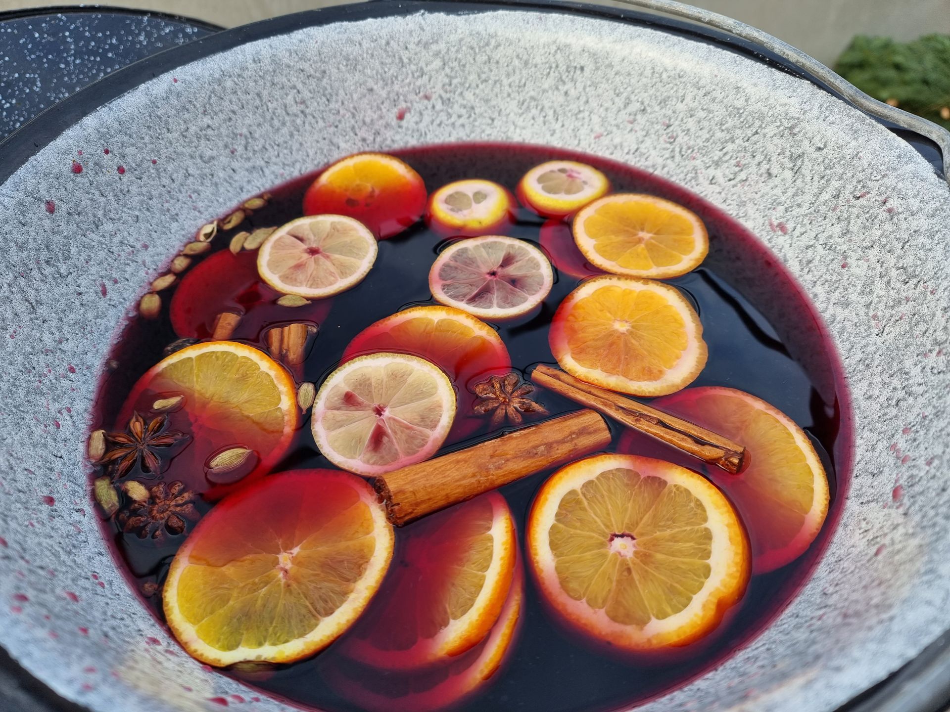 Glühwein in een grote metalen pot, met schijfjes sinaasappel en citroen, kaneelstokjes en steranijs.