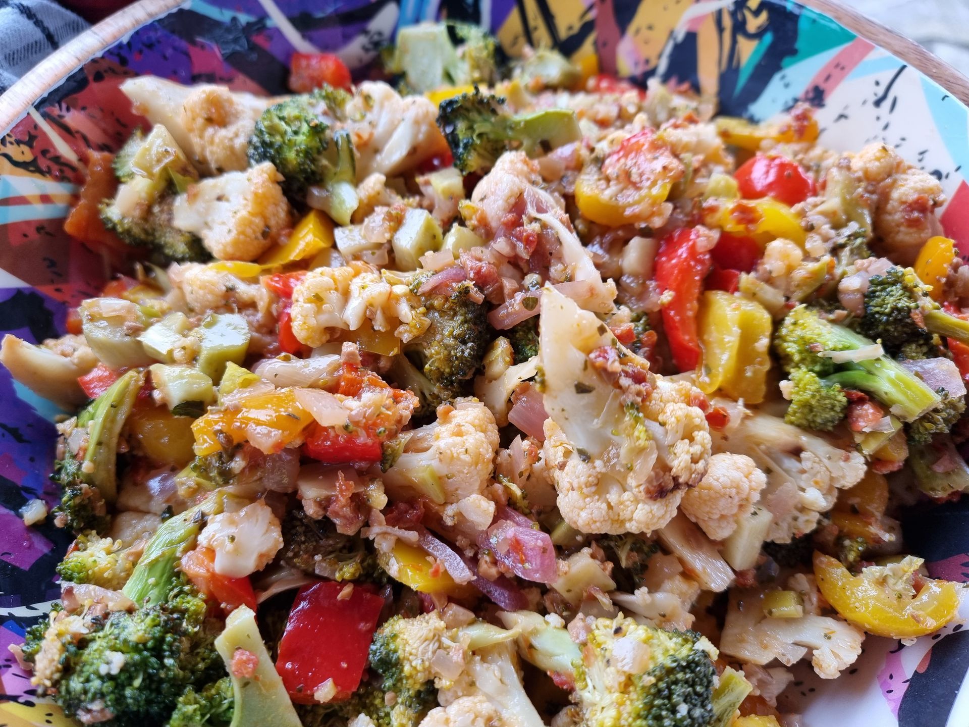 Een kom geroosterde groenten: bloemkool, broccoli, rode en gele paprika's, gemengd met kruiden.