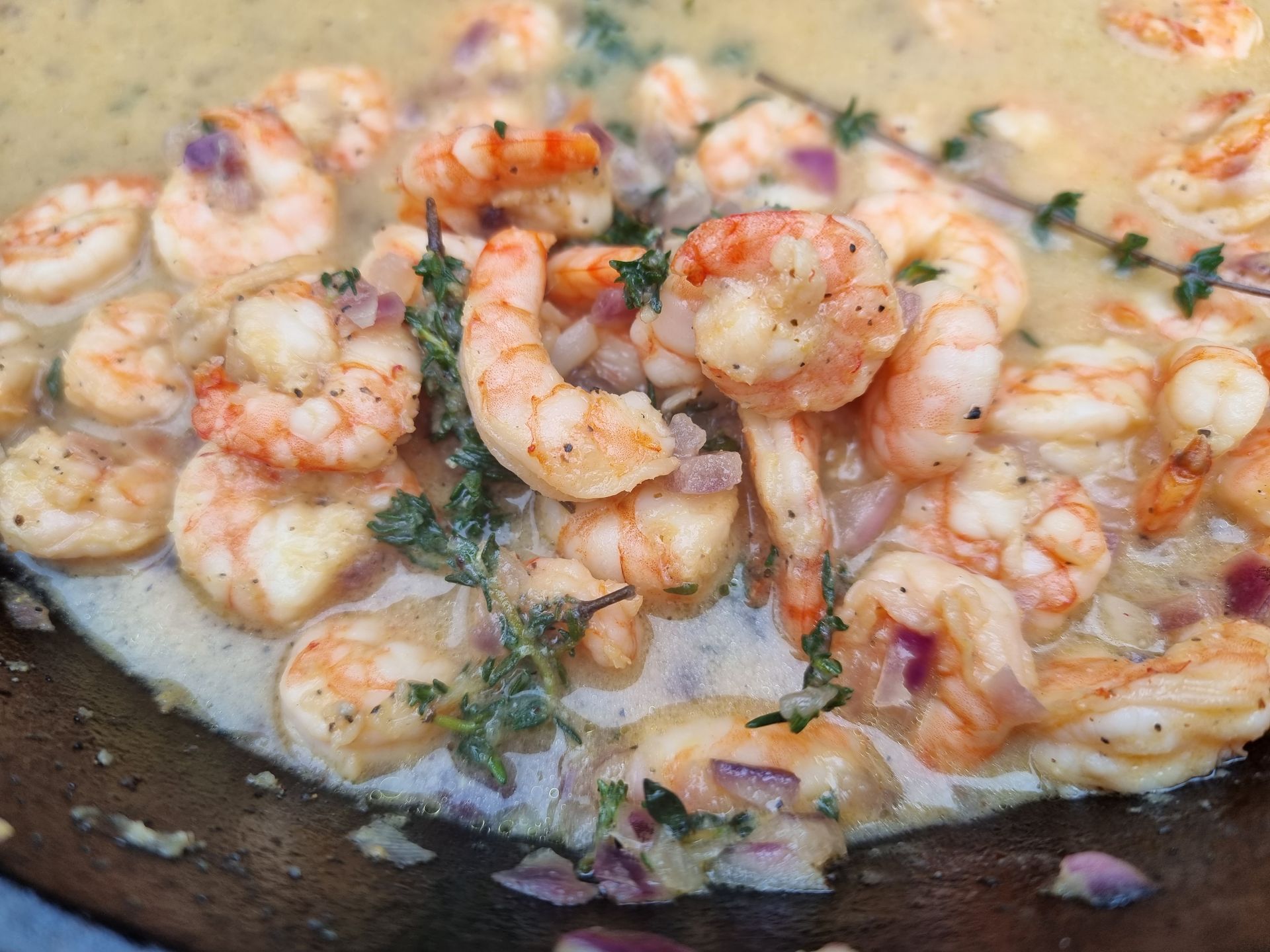 Garnalen in een romige saus met kruiden en rode ui, gebakken in een pan.