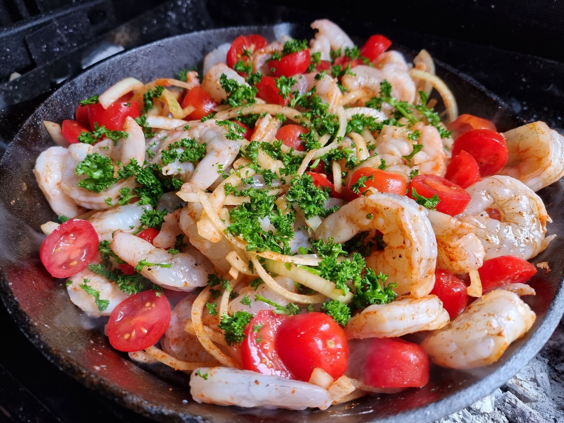Garnalen en cherrytomaten in een pan, gegarneerd met peterselie en kruiden, en vervolgens gegrild.