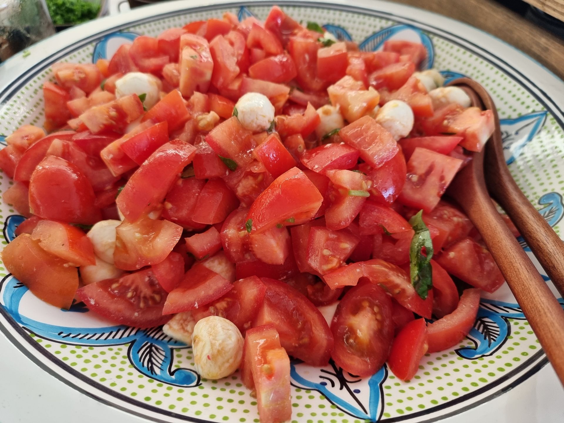 Salade van tomaat en mozzarella in een decoratieve kom met houten serveerlepels.