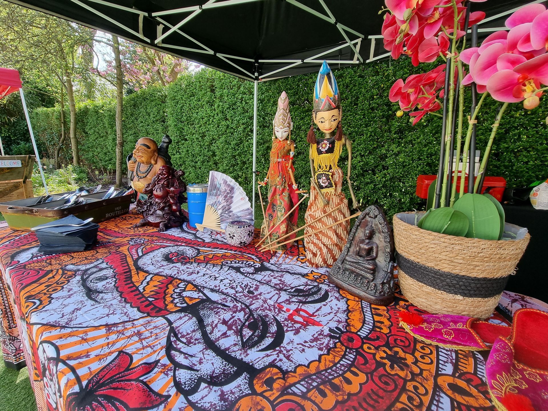 Tafel met Indonesische handwerkproducten en bloemen onder een afdak in de buitenlucht.