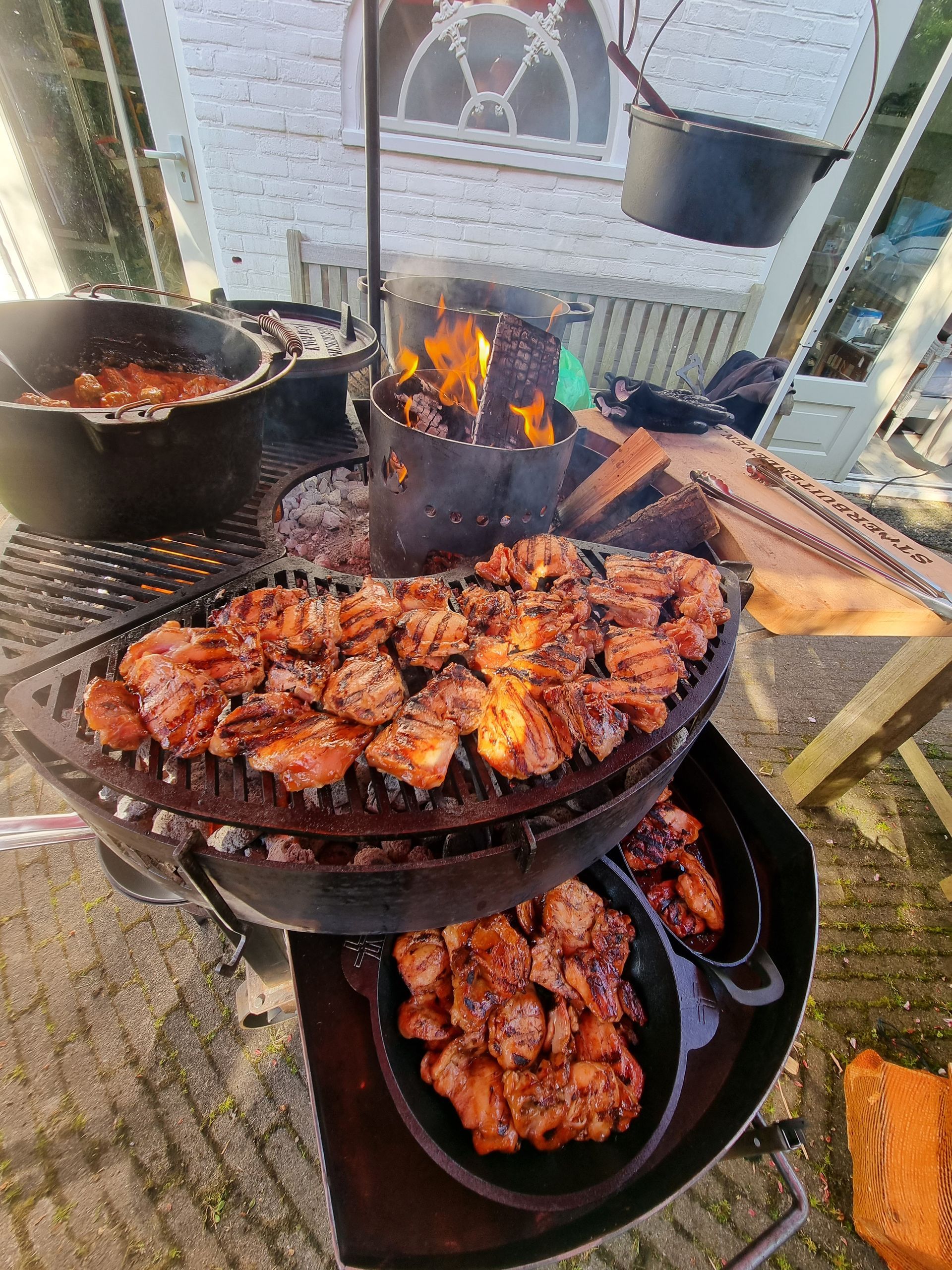 Gegrilde kip die op een grill wordt bereid, samen met andere kookpannen en een kolenstarter.