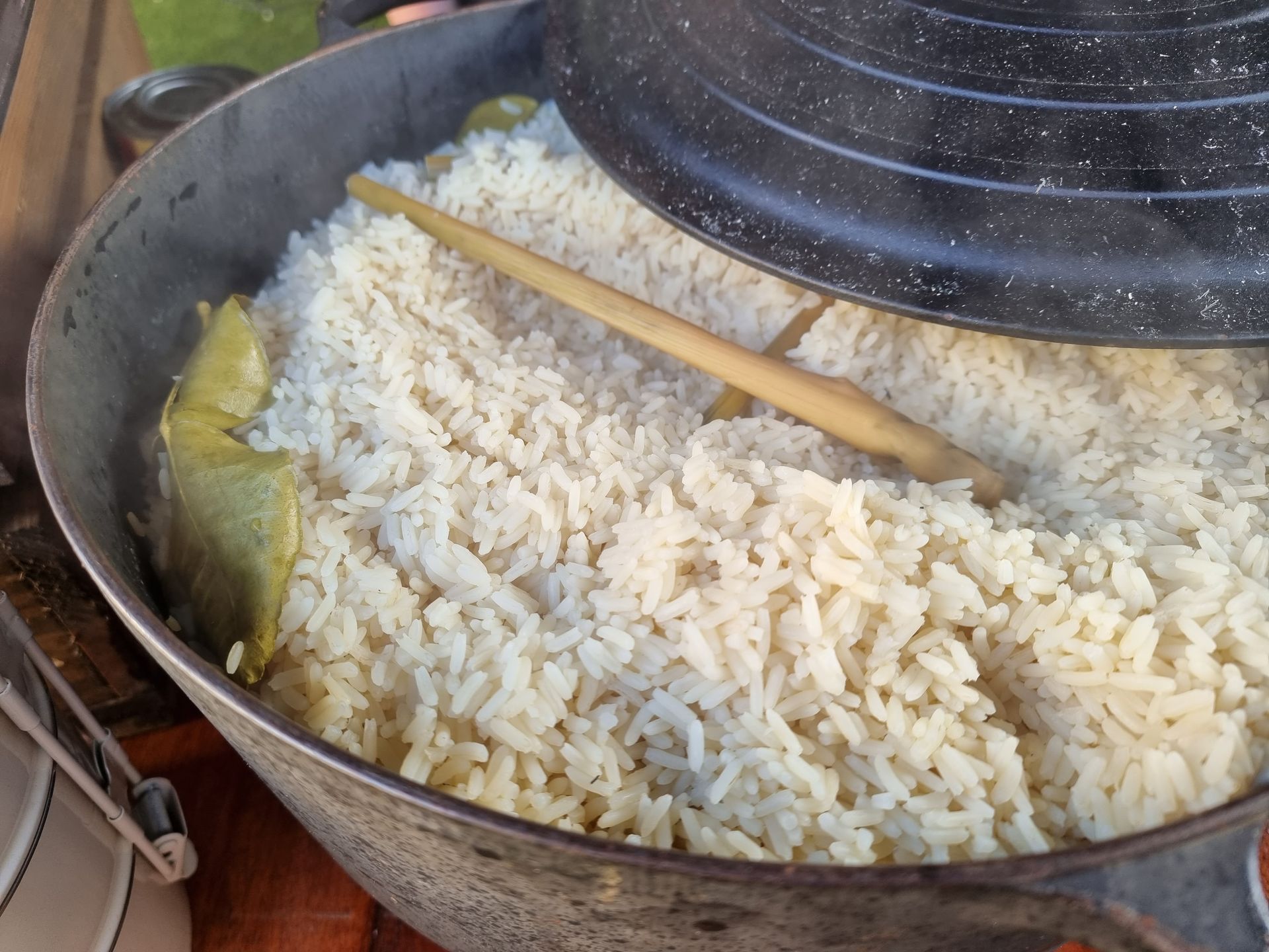 Gekookte witte serehrijst in een pan met een deksel dat een klein beetje openstaat, met een houten lepel.