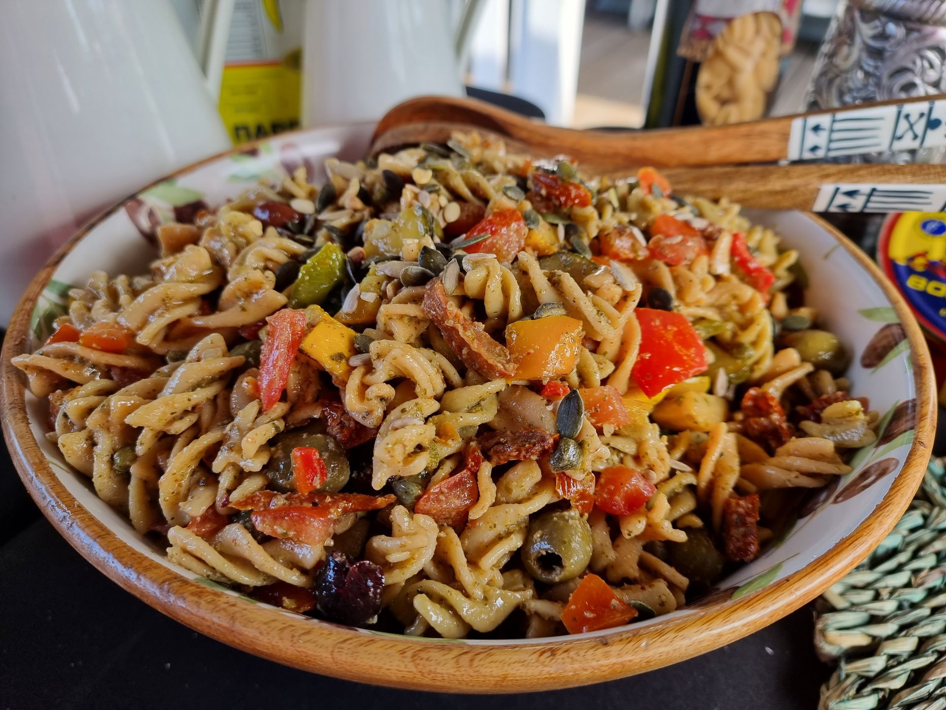 Pastasalade met olijven, tomaten en groenten in een kom, geserveerd met houten lepels.