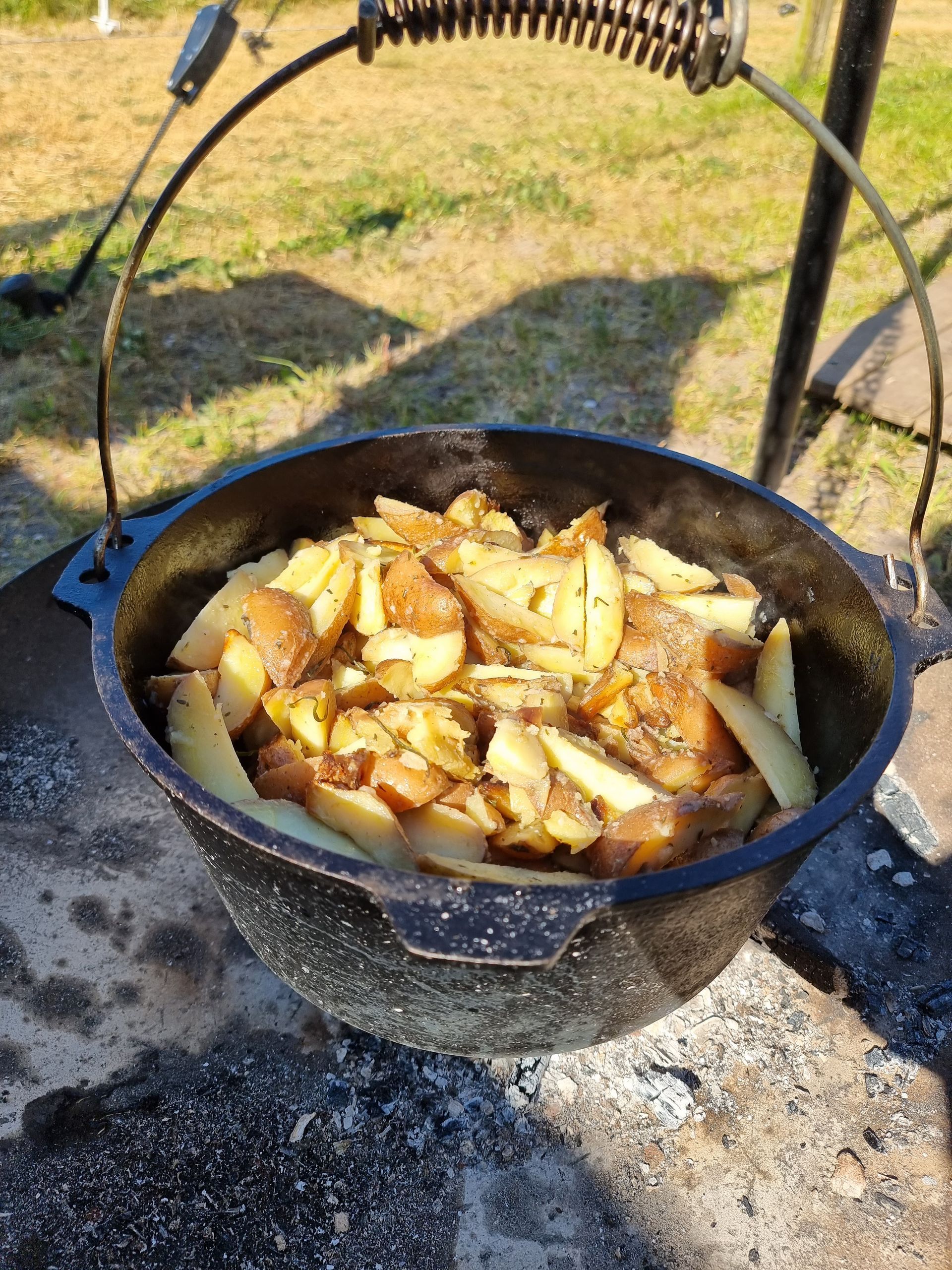Aardappelen bakken in een Dutch oven in de buitenlucht, de pot hangt boven een vuur.