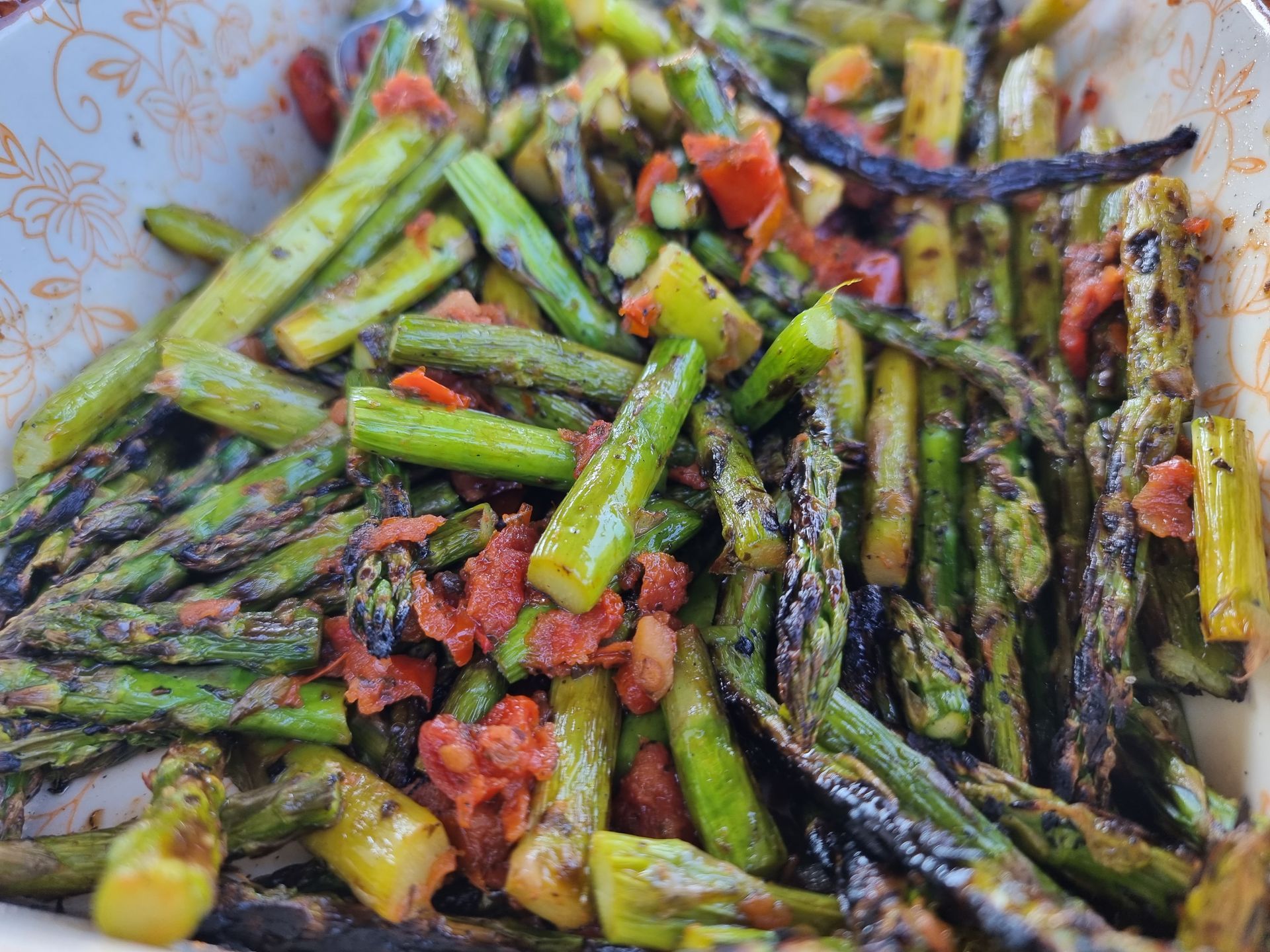 Gegrilde asperges met rode tomaten in een witte kom.