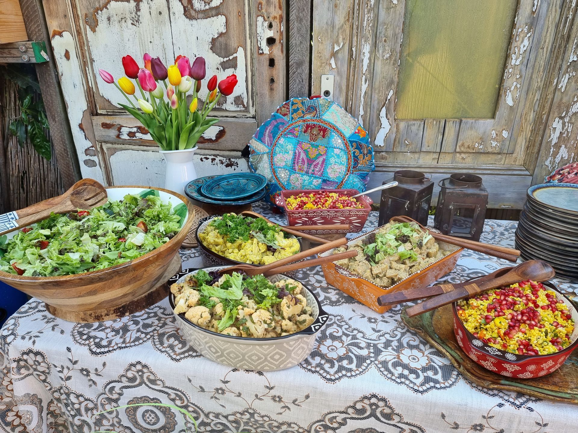 Buffettafel met diverse kleurrijke schalen met eten, een vaas met tulpen, tegen een achtergrond van verweerd hout.