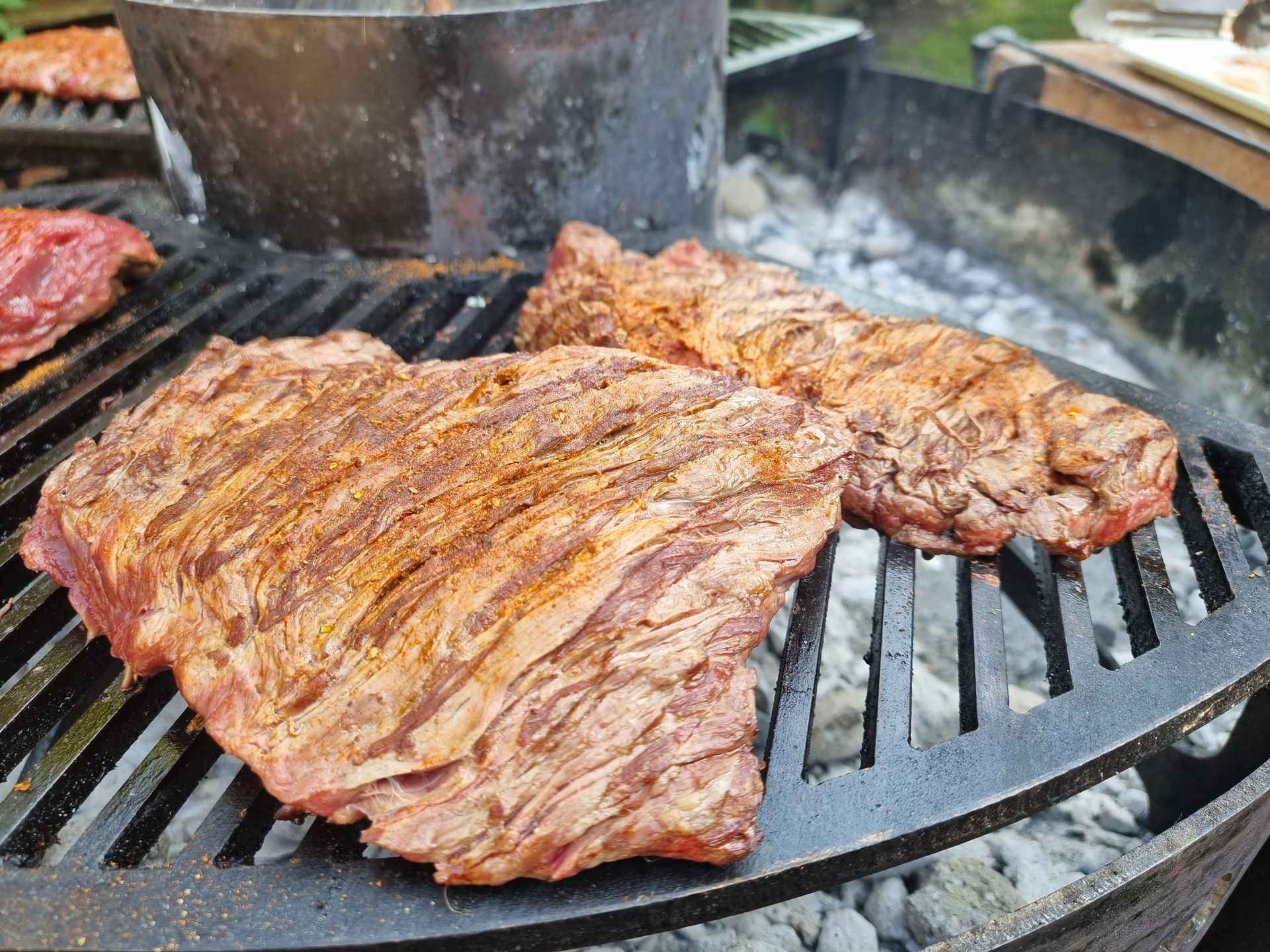 Twee gekruide stukken bavette die op een houtskoolgrill worden gegrild.