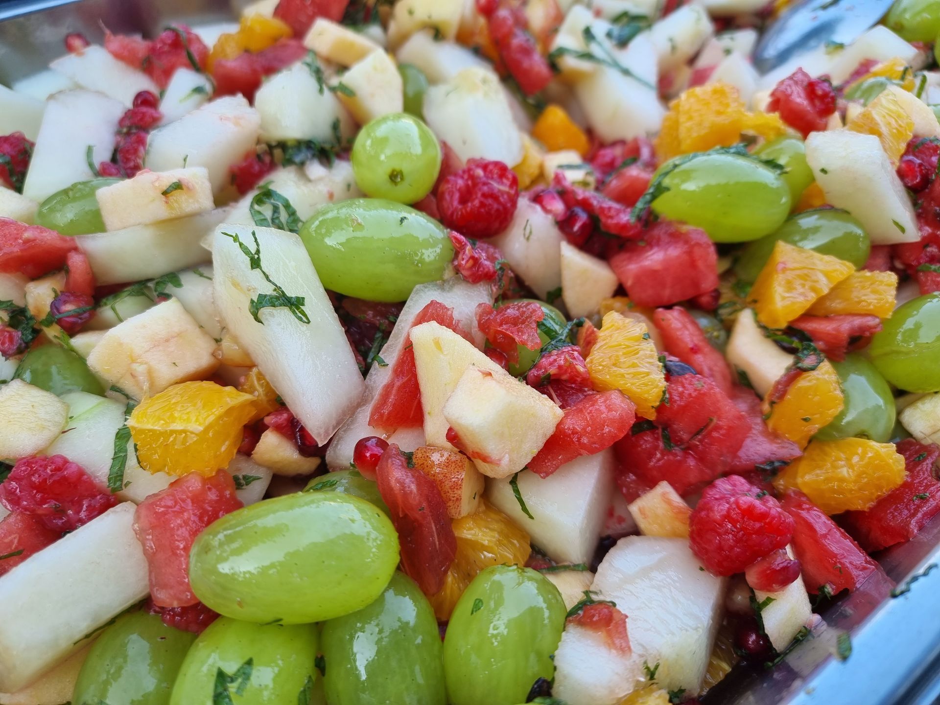 Fruitsalade met groene druiven, frambozen, stukjes sinaasappel en plakjes peer.