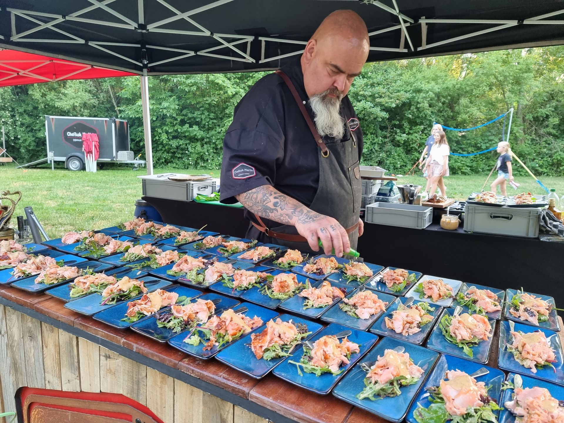 Chefkok Martin serveert warm gerookte zalm op blauwe borden, evenement in de buitenlucht.