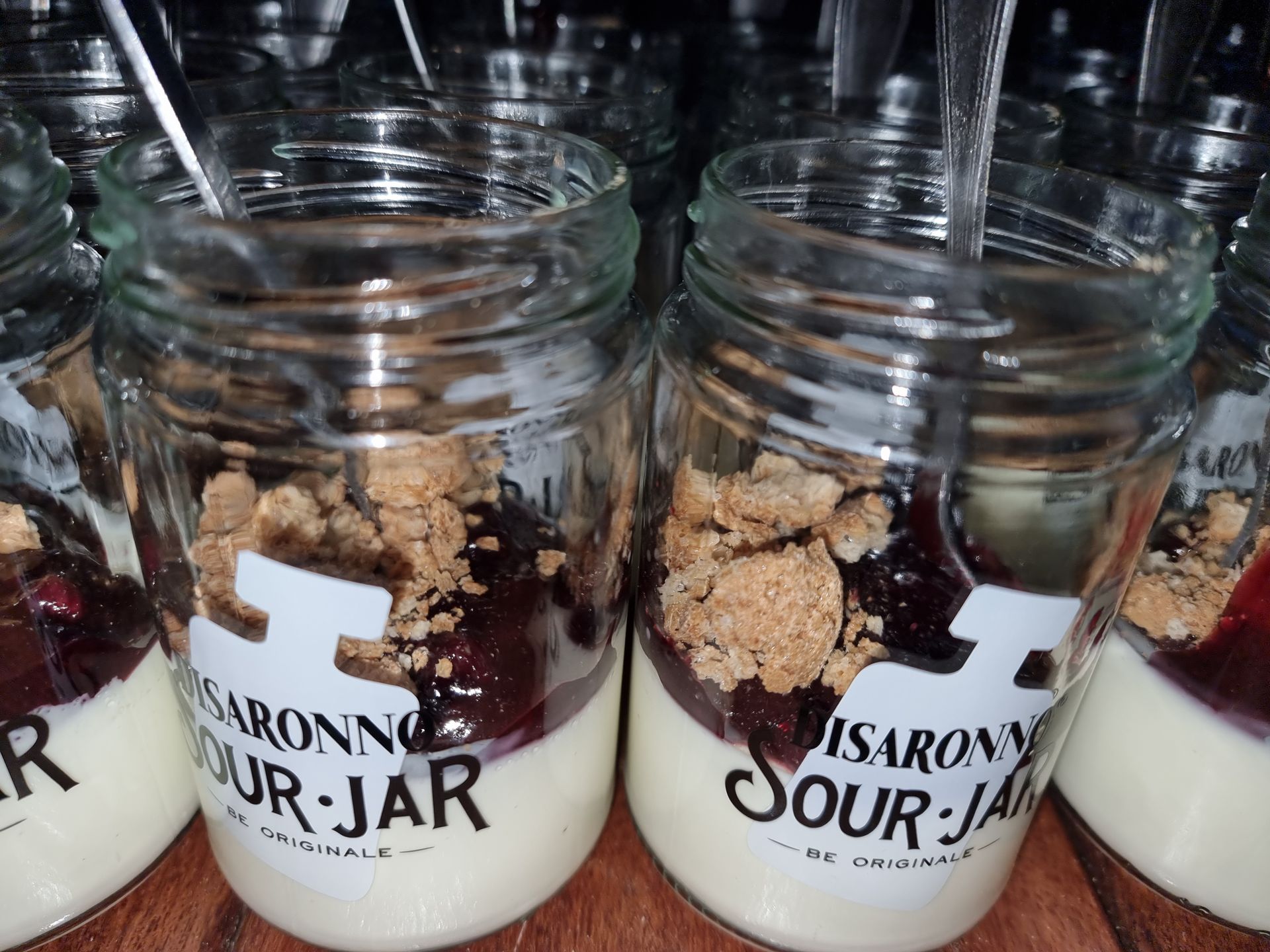 Desserts in potjes: laagjes romig wit gebak, rode compote en koekkruimels; etiket 
