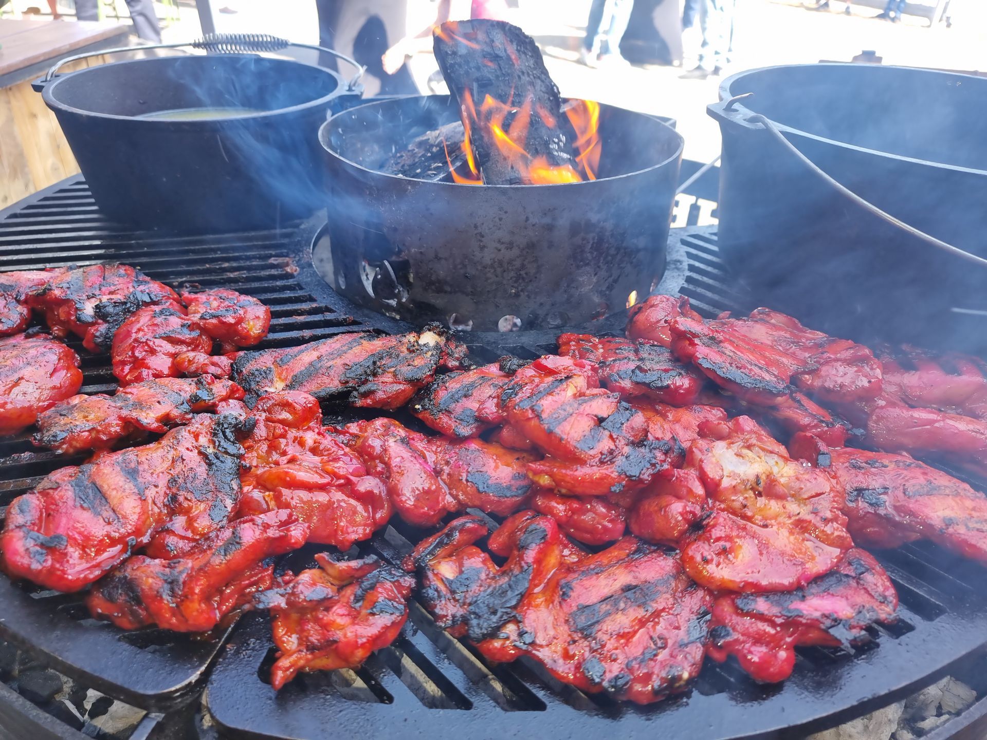 Gegrild red roast chicken op een grill met een vuurplaats in het midden; er staan ​​ook twee zwarte braadpannen.