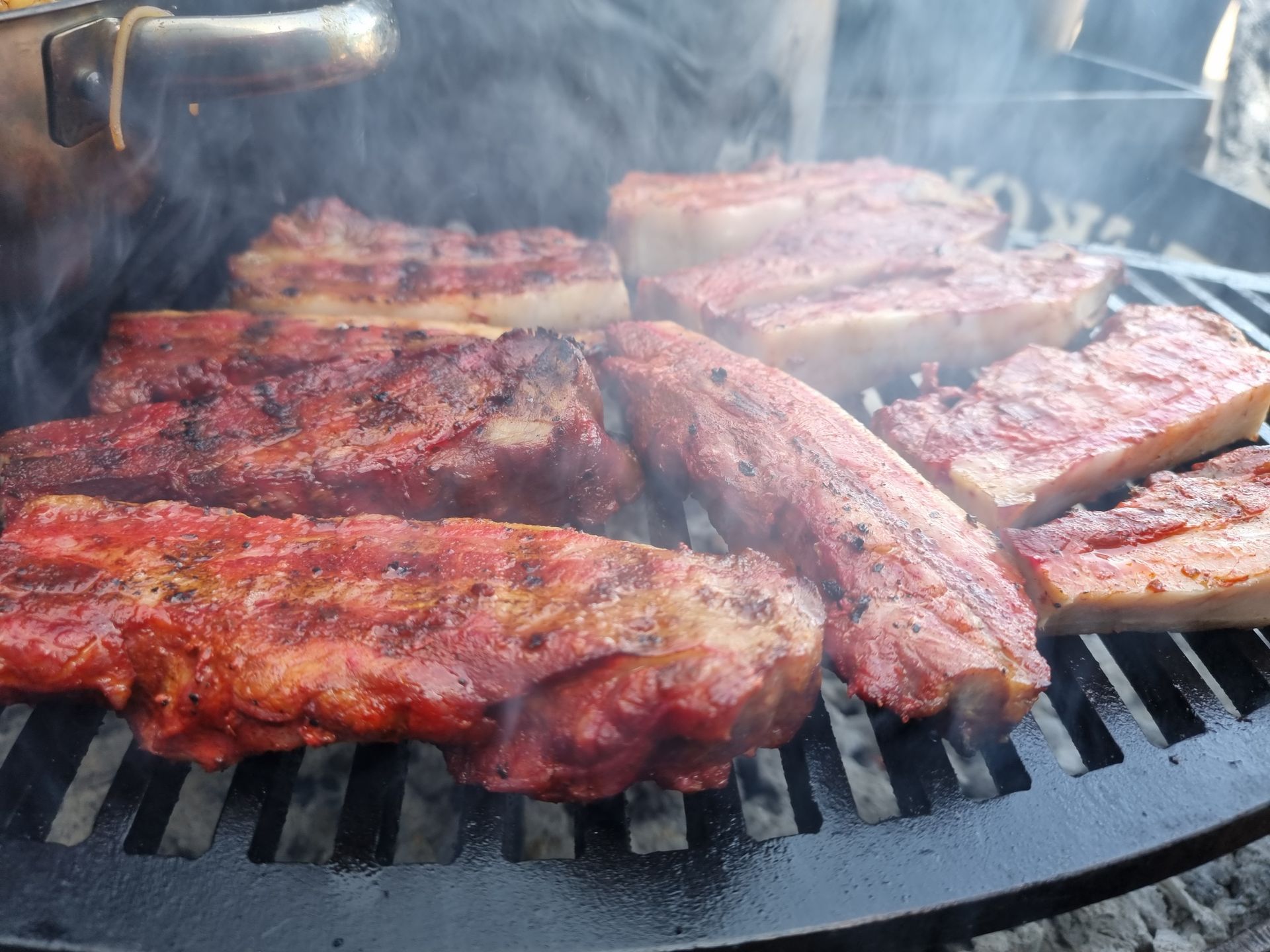 Close-up van buikspek die gegrild wordt op een zwarte, ronde grill, met zichtbare rook.