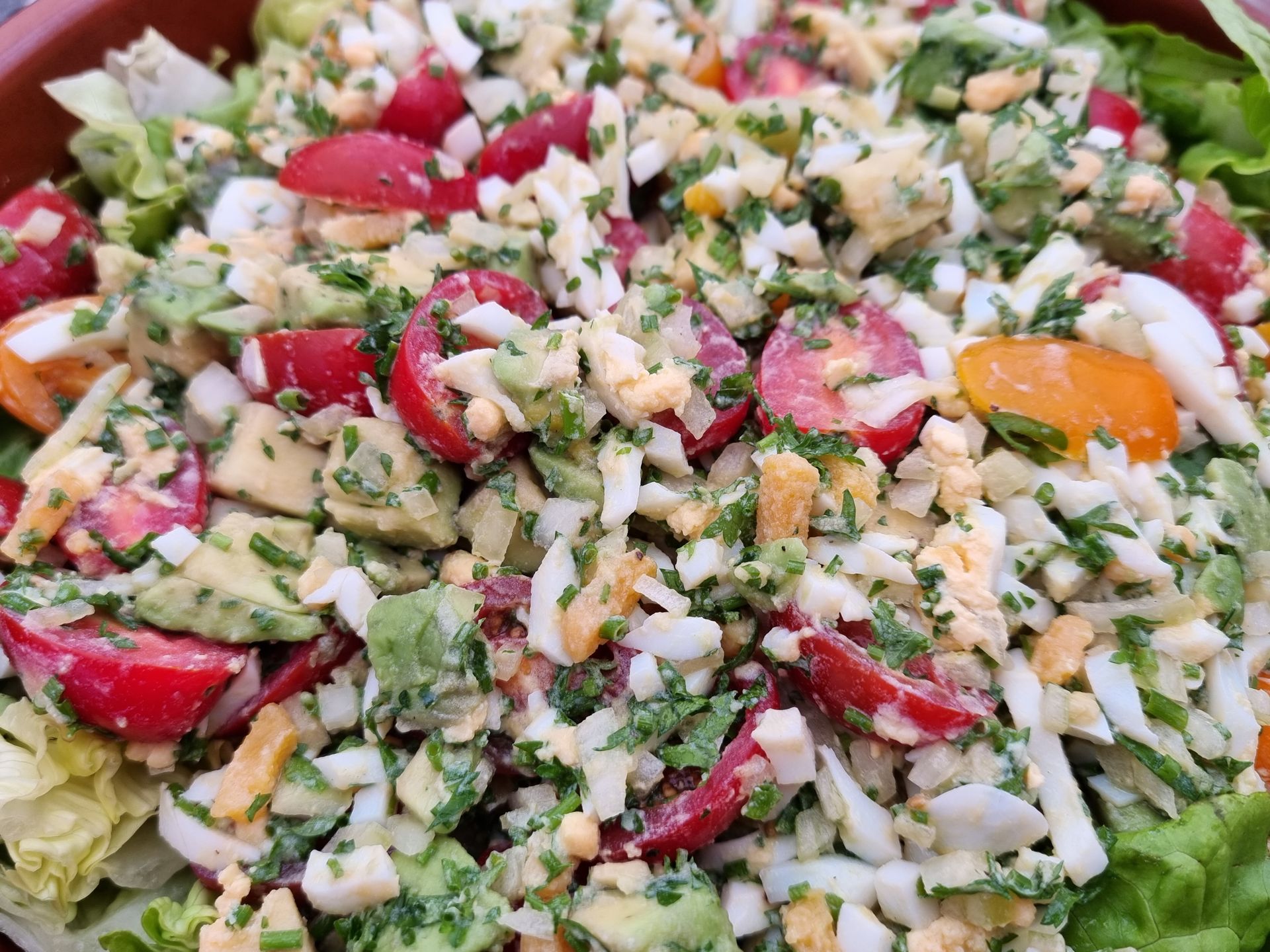 Salade met in blokjes gesneden avocado, gehalveerde cherrytomaatjes, gehakte eieren en kruiden.