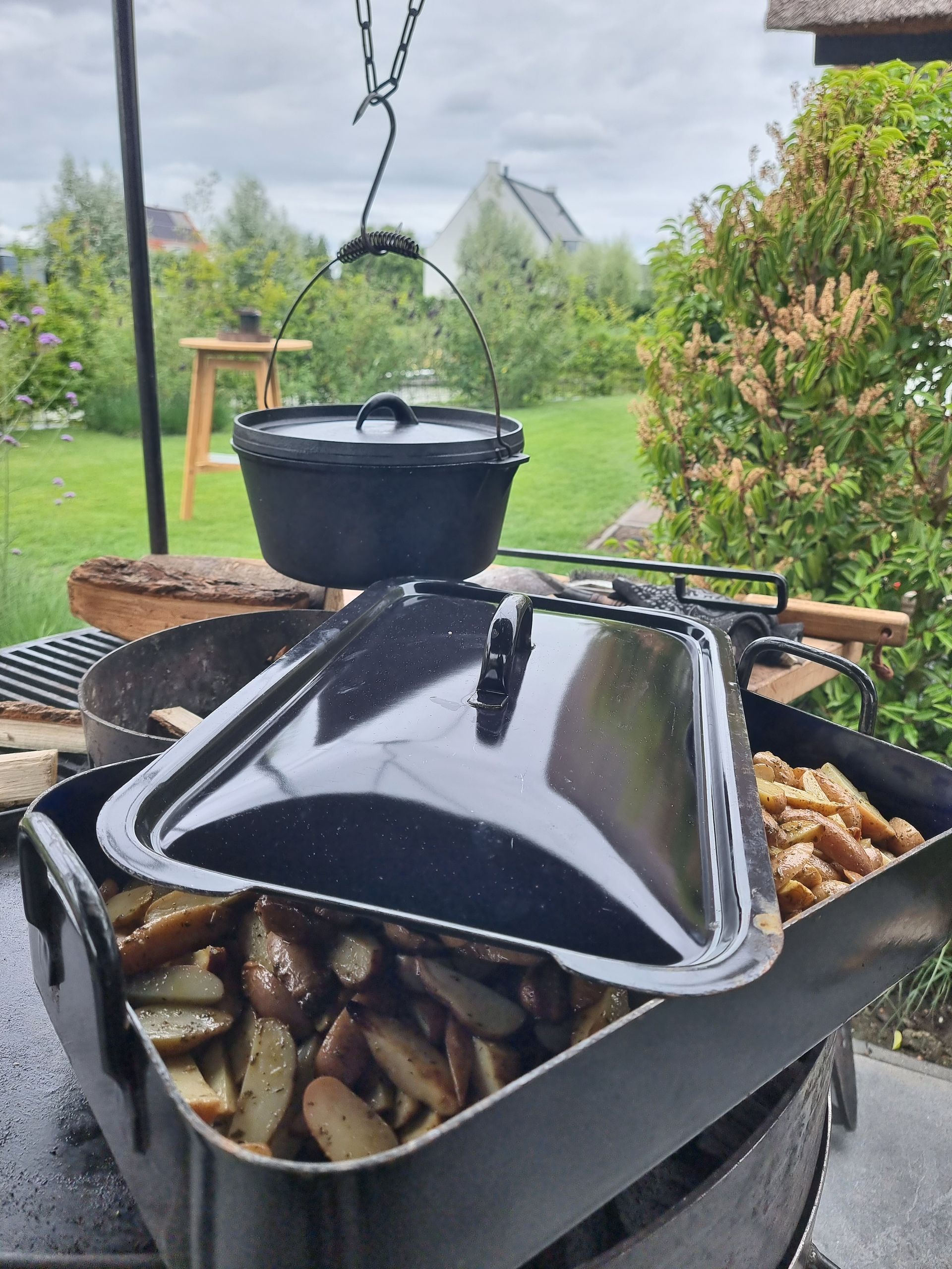 Buitenkeuken met hangende gietijzeren pot en schaal boven de kolen.