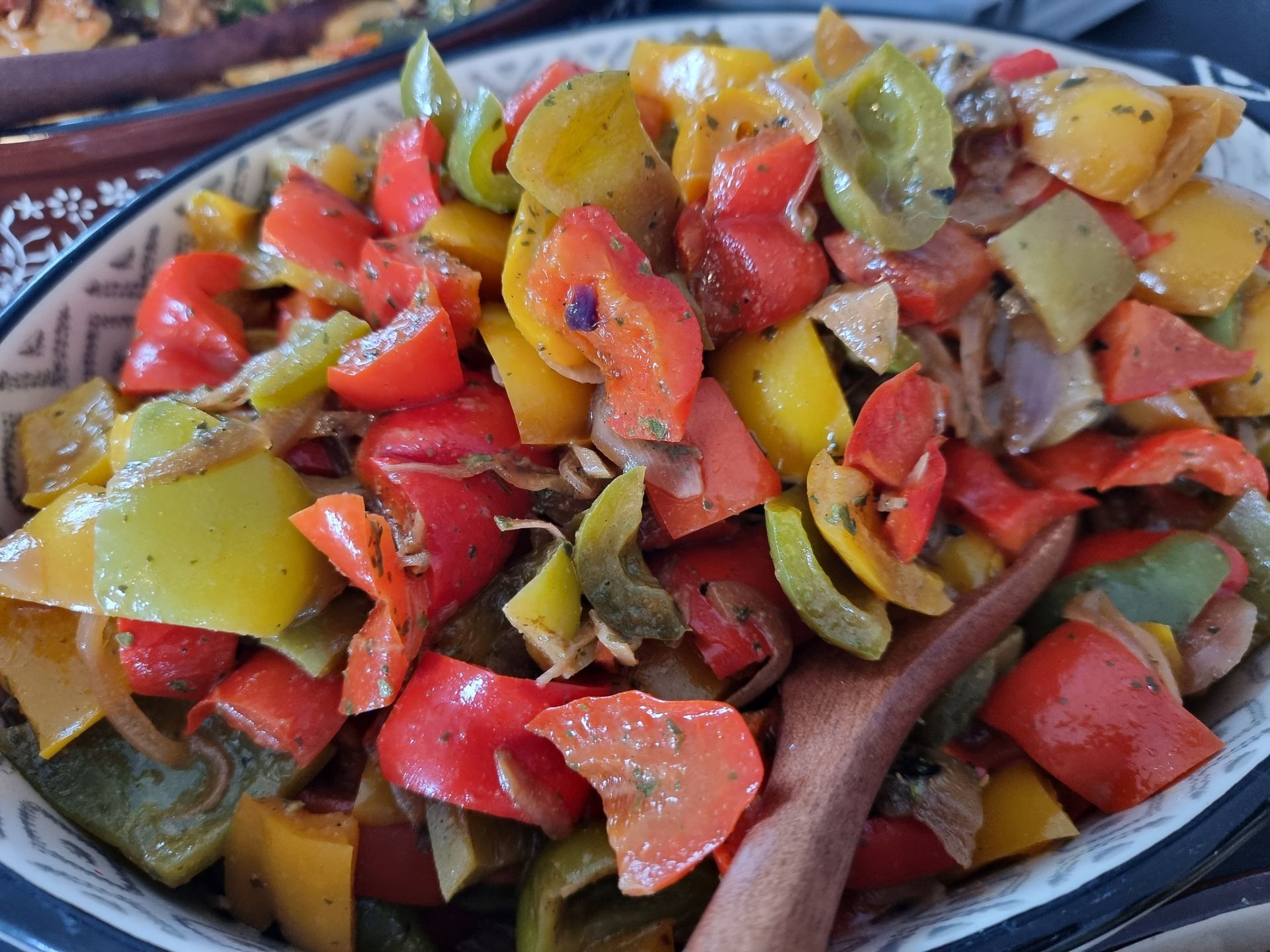 Kleurrijke paprika's, rood, geel en groen, in een serveerschaal met een houten lepel.