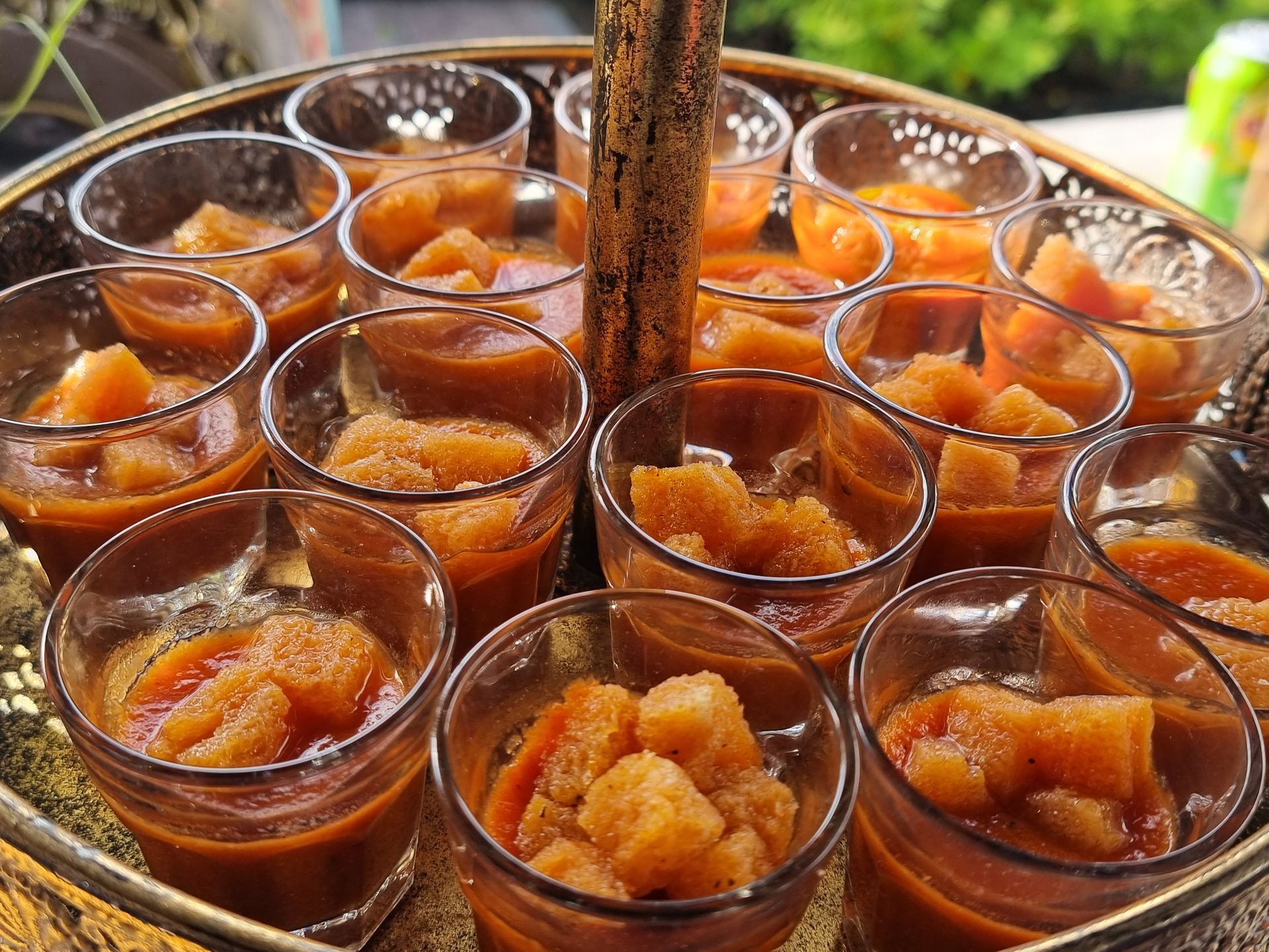 Een arrangement van kleine glazen kopjes gevuld met een soep met croutons, gepresenteerd op een etagère.