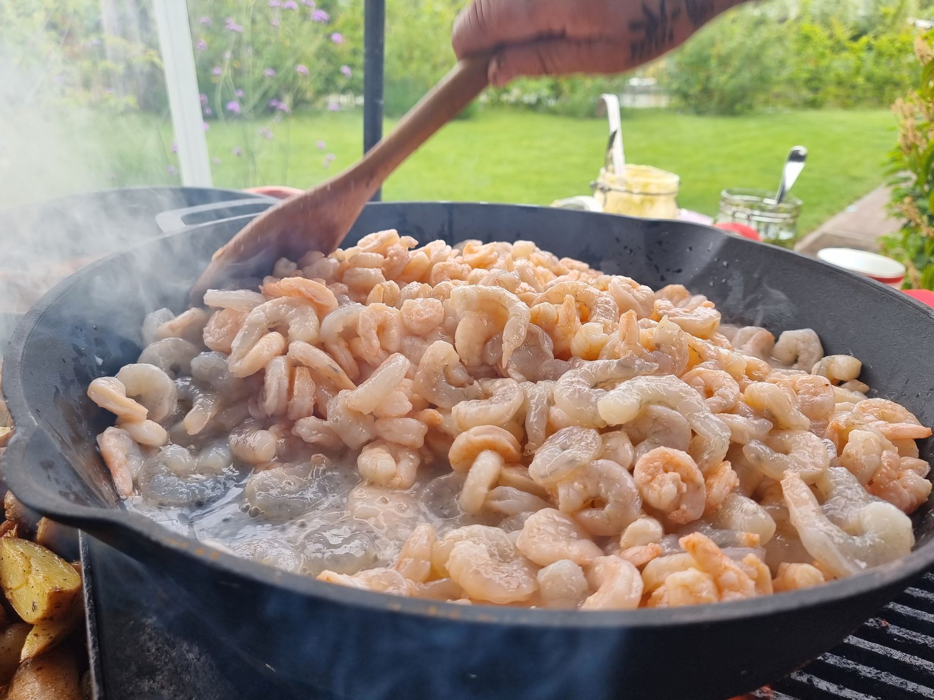 Garnalen worden buiten in een grote pan gebakken en met een houten lepel geroerd. Er stijgt stoom op.