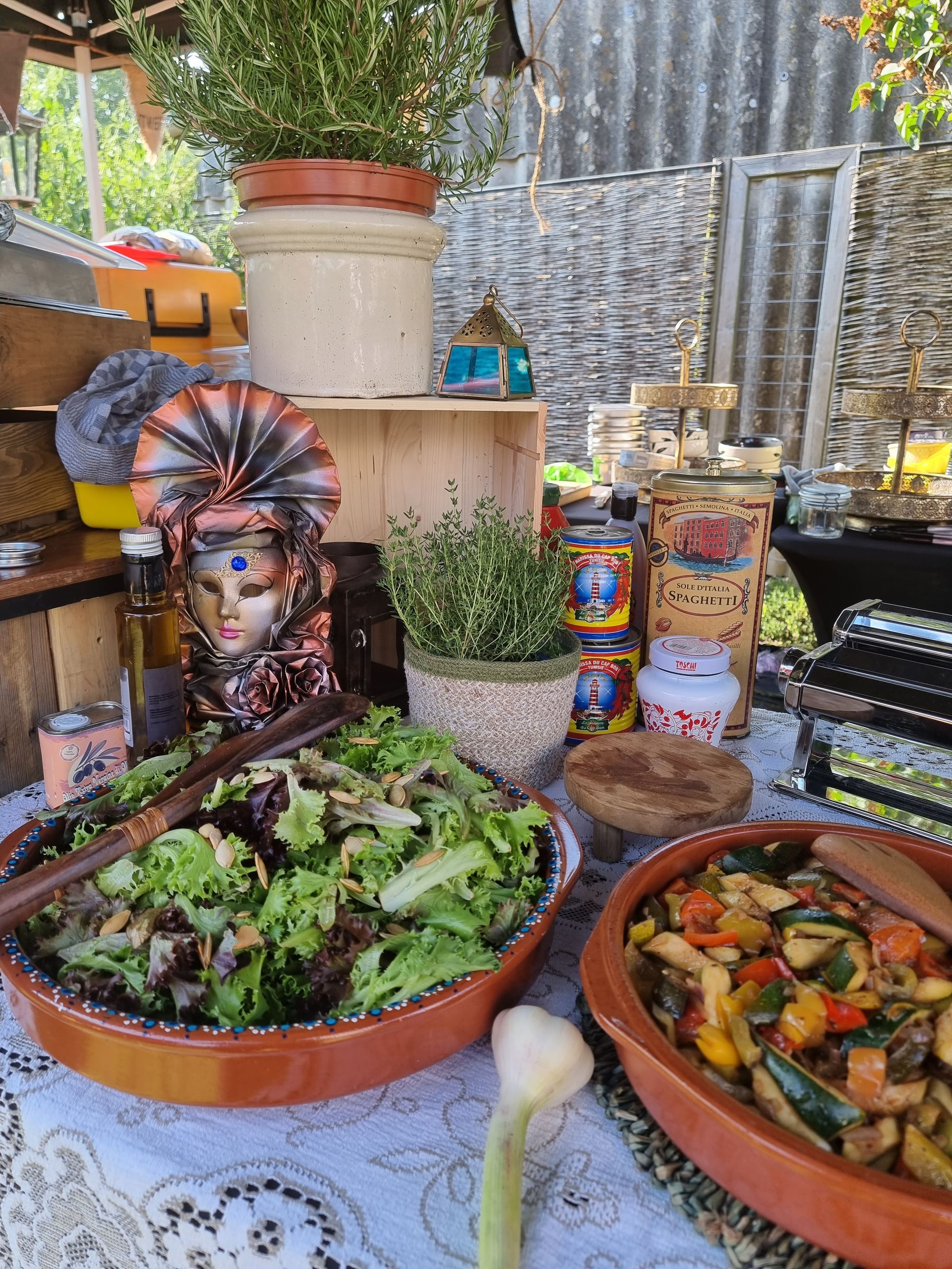 Salades en groentegerechten op een tafel versierd met planten, een Venetiaans masker en andere Italiaanse voorwerpen.