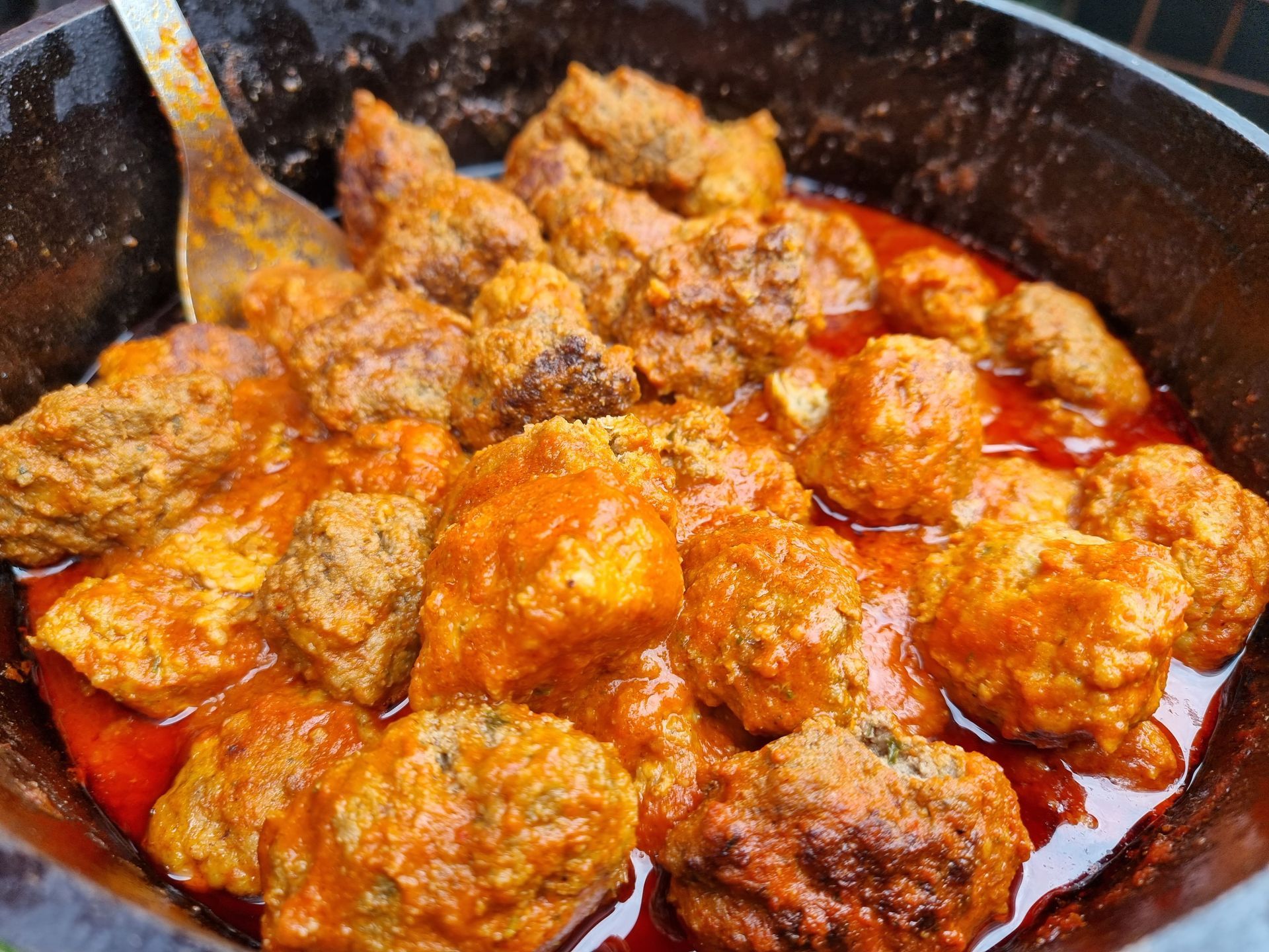 Gehaktballetjes in een rood-oranje saus in een gietijzeren kookpot.