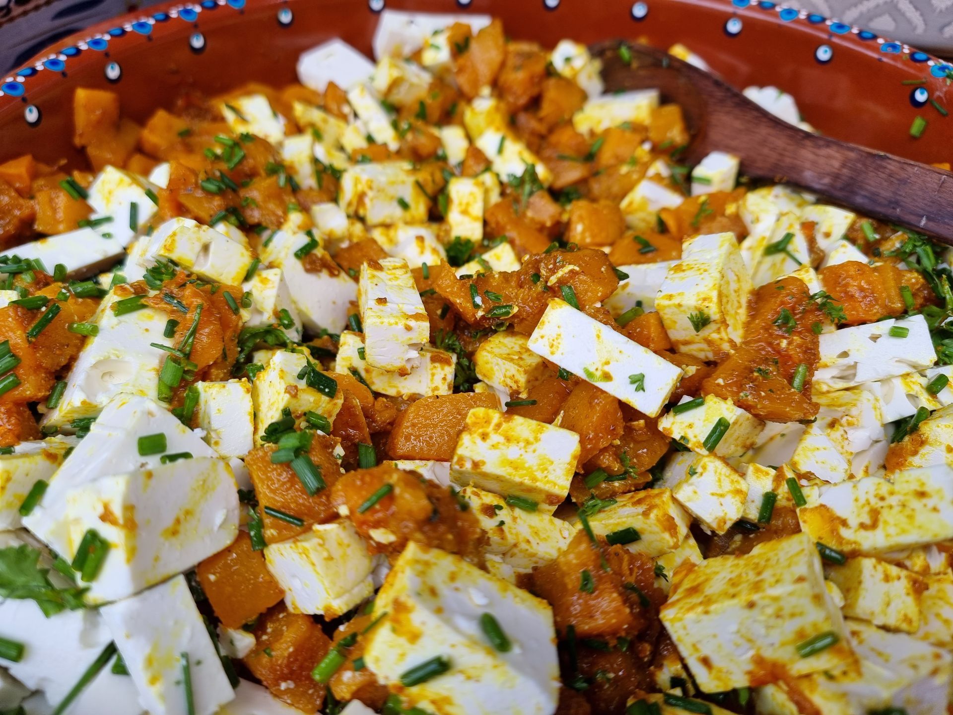 Een kom met blokjes pompoen en feta, gekruid met bieslook.