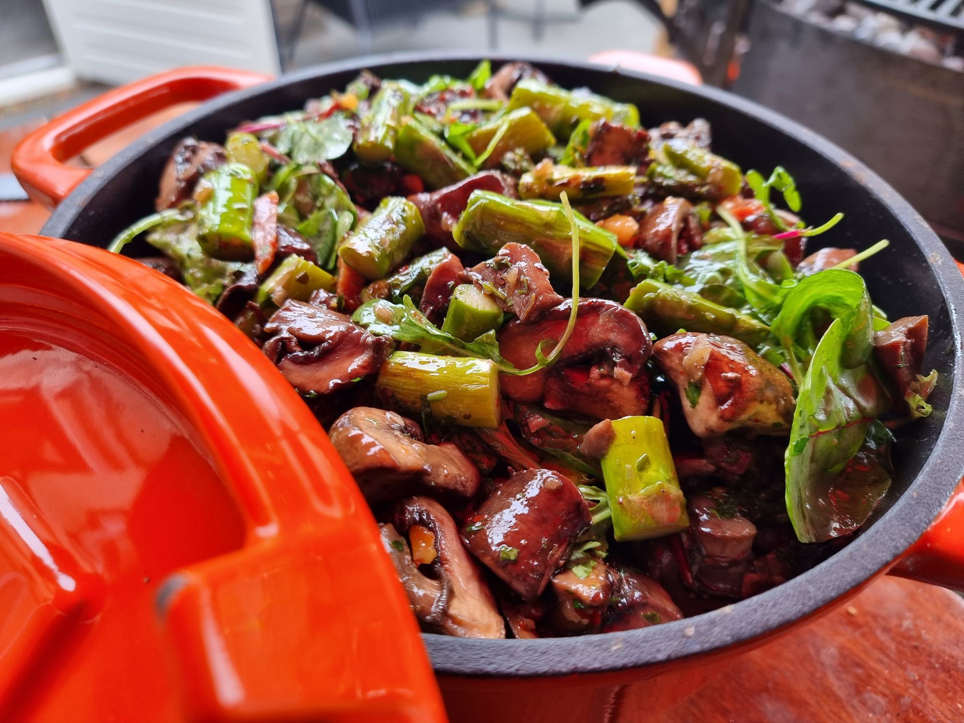 Gestoofde champignons en groene asperges in een oranje Dutch oven, met kruiden.