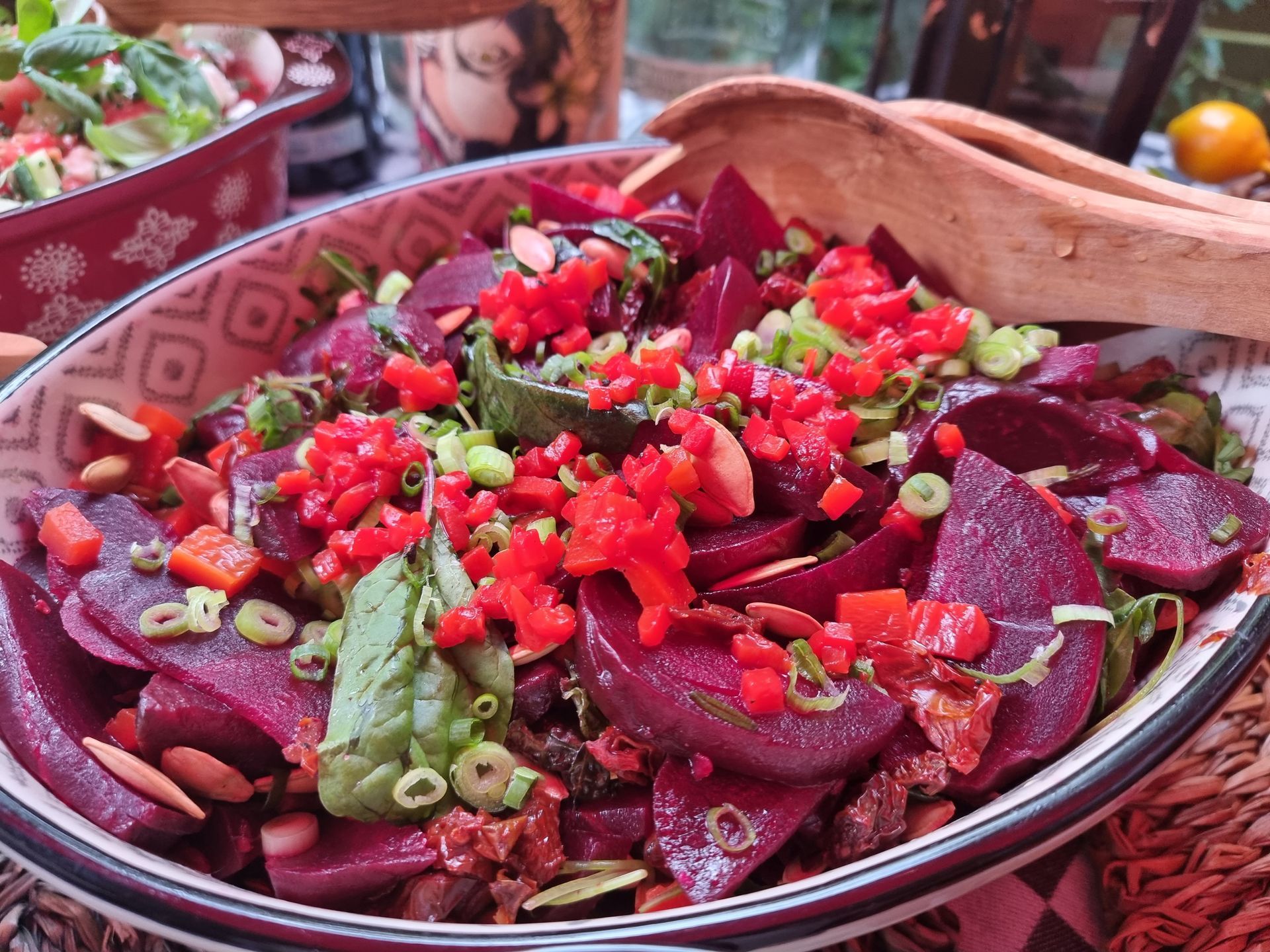 Bietensalade in een kom met patroon, gegarneerd met rode paprika, groene uien en amandelen.
