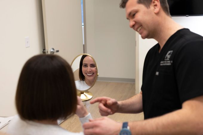 A man is pointing at a woman 's face in a mirror.