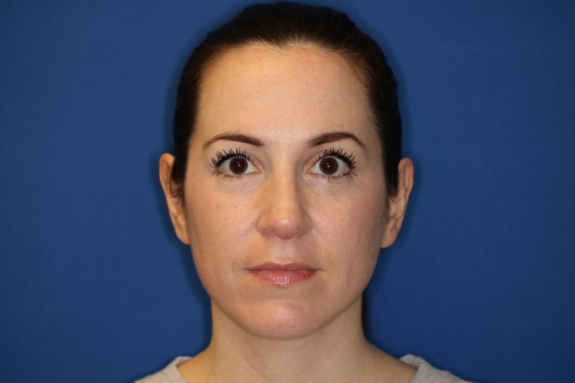 A woman is standing in front of a blue background and looking at the camera.