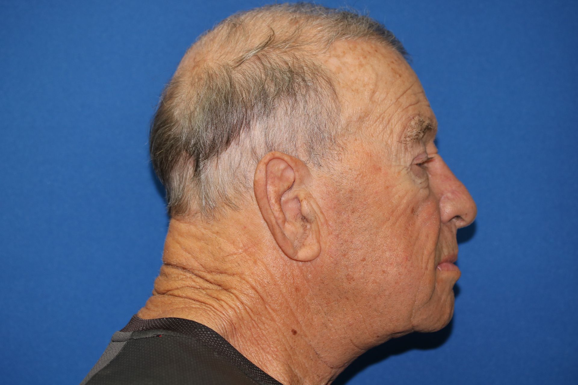 A man with a shaved head is standing in front of a blue background.