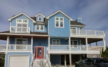 Blue two-story beach house with white railings, balconies, and red front door.