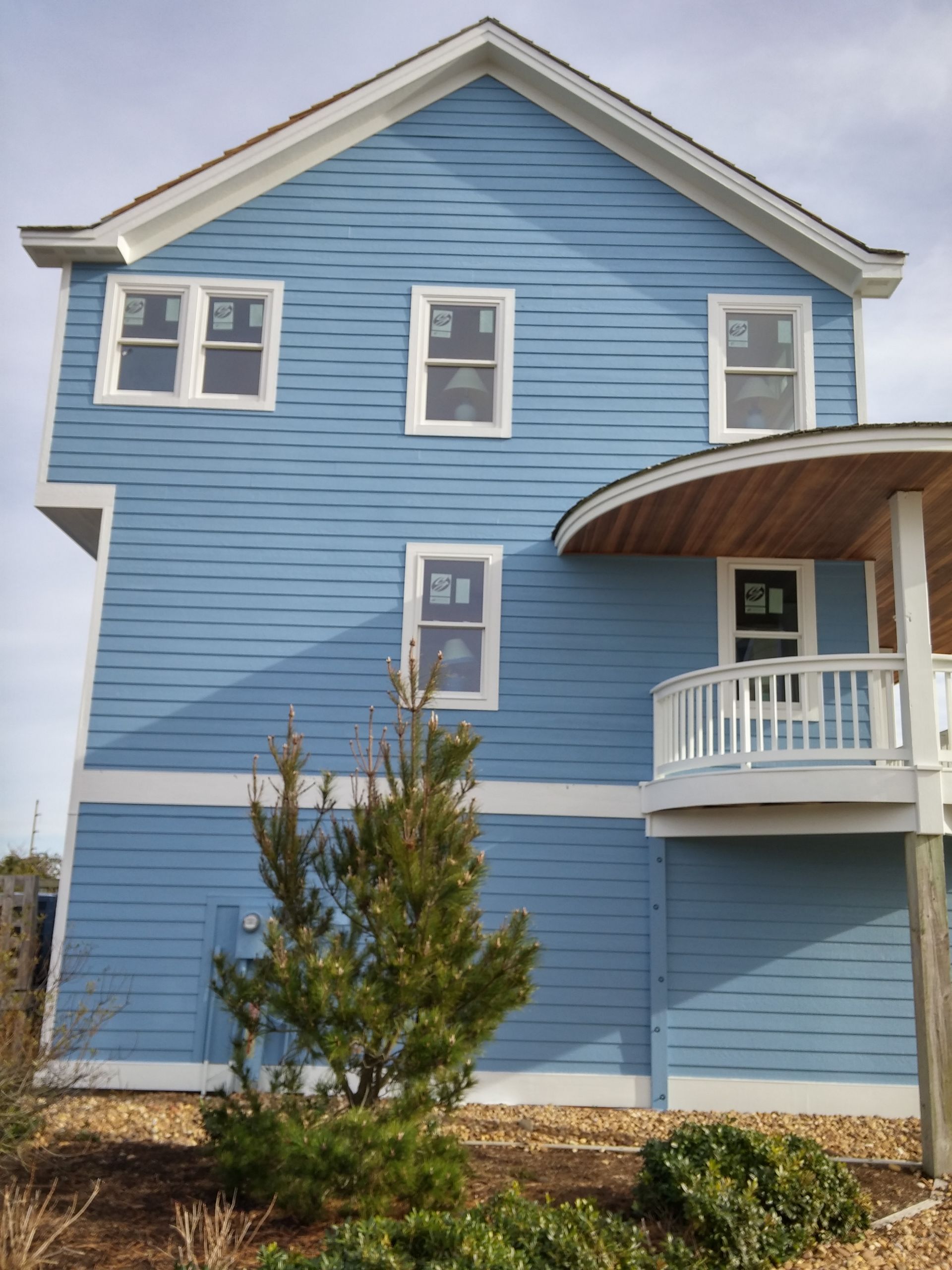 Blue house with white trim, windows, and curved porch, against a cloudy sky.
