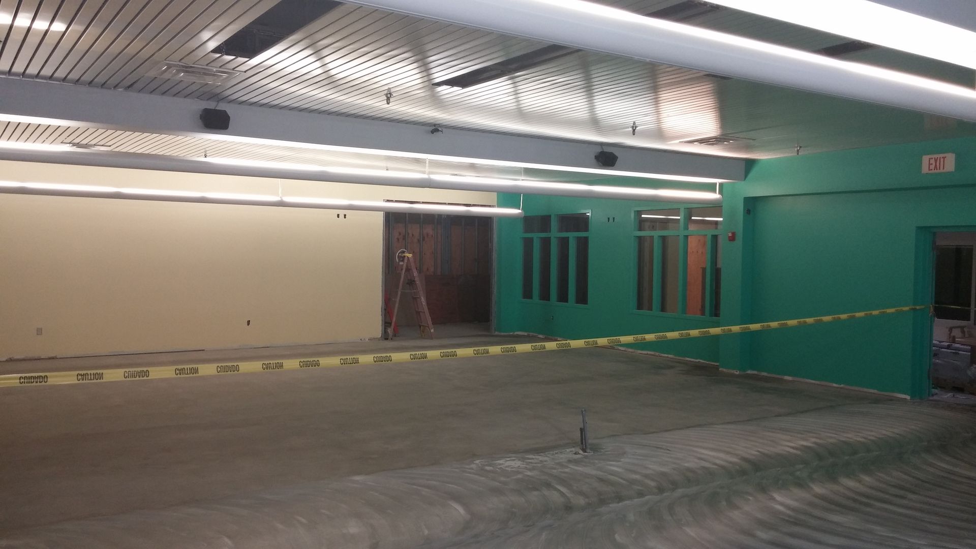 Construction site interior with green walls, caution tape, and concrete floor.
