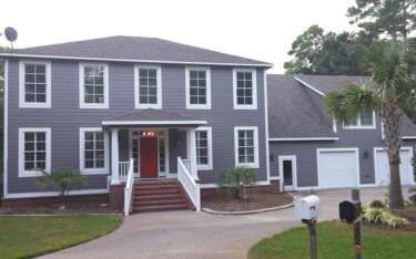 Gray house with white trim, red door, and a circular driveway.