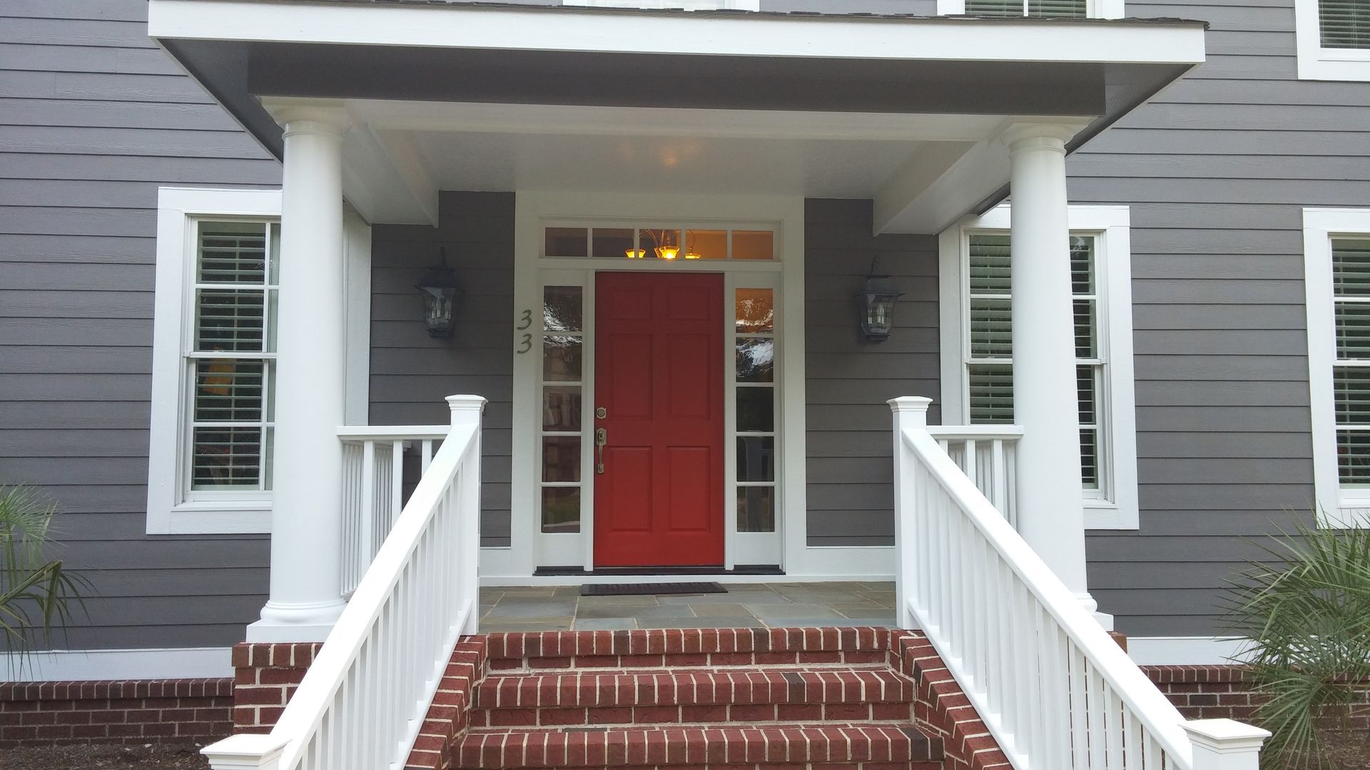Gray house with a red front door, white pillars, and brick steps.