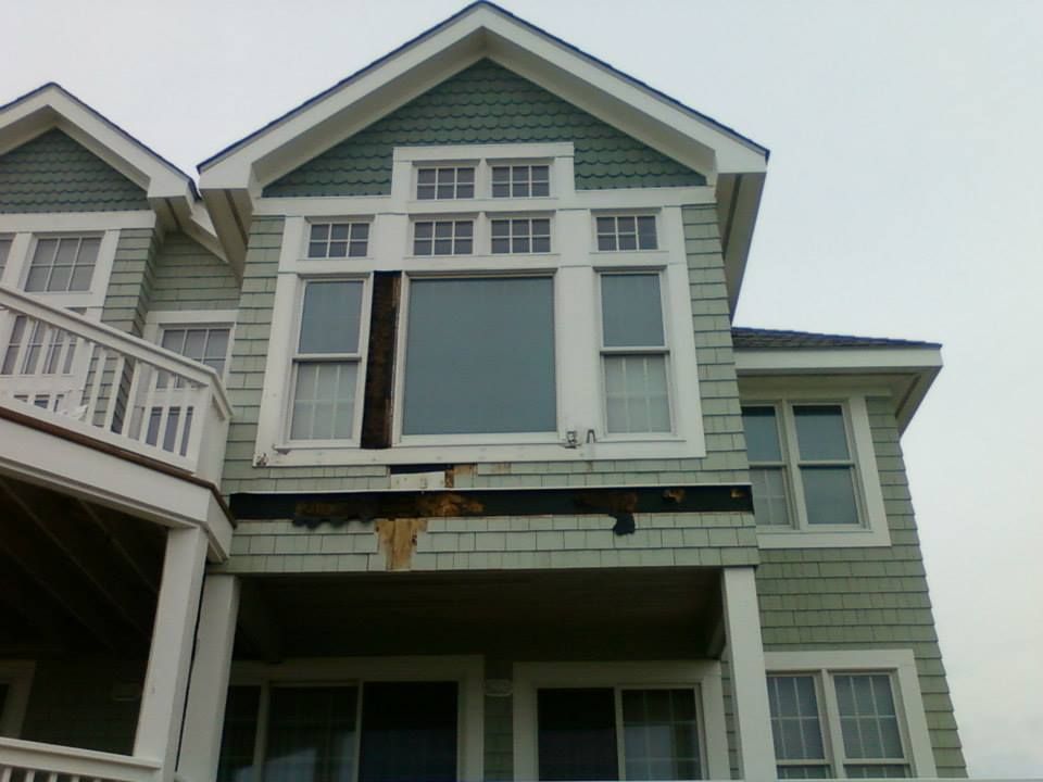 Exterior of a two-story house with damaged siding and windows. Green shingles, white trim, and a partially open window.