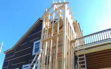 House under construction with exposed wooden frame against blue sky.