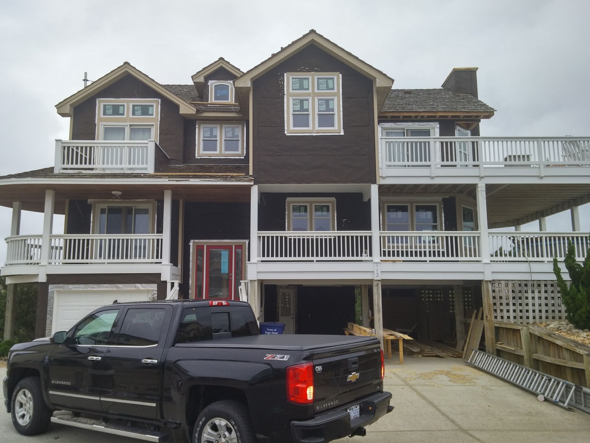 Dark brown house with white balconies, black truck in front. Cloudy day.