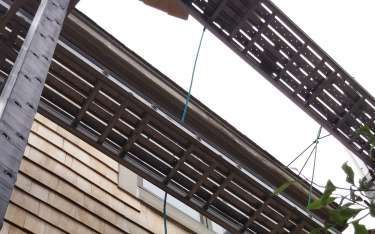 Wooden slats shade a building facade with cedar siding, with glimpses of sky.