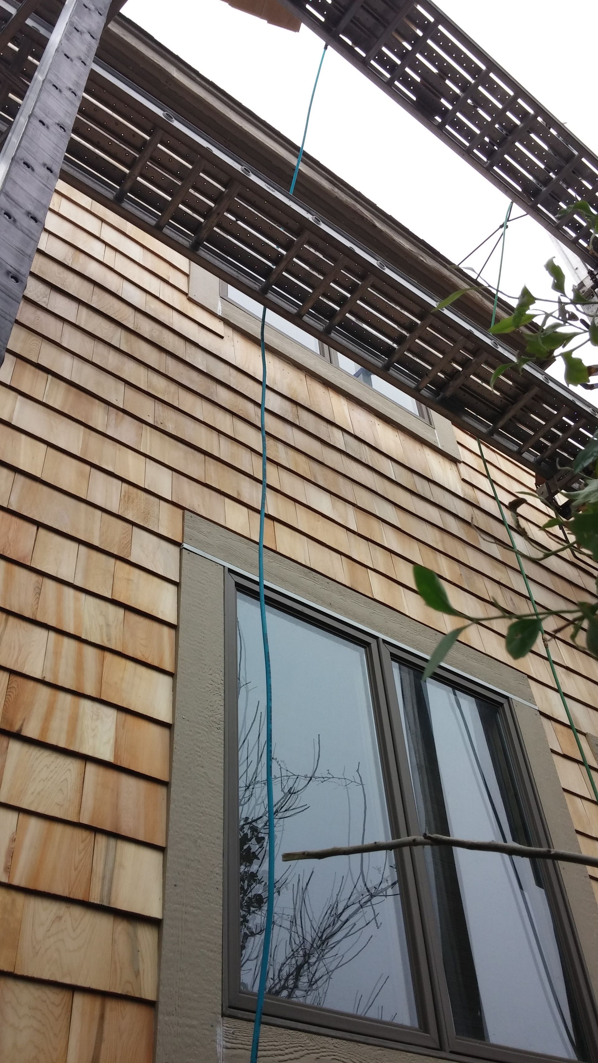 Exterior view of a building with wood siding, a window, and a metal structure overhead. A rope hangs down.