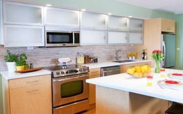 Modern kitchen with light wood cabinets, stainless steel appliances, and a white countertop island.