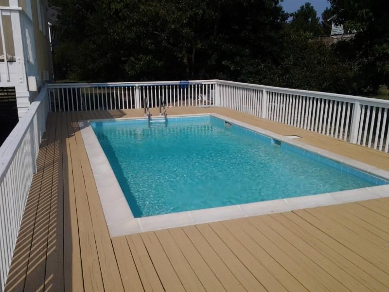 Pool surrounded by a wooden deck with white railing. Turquoise water reflects sunlight.