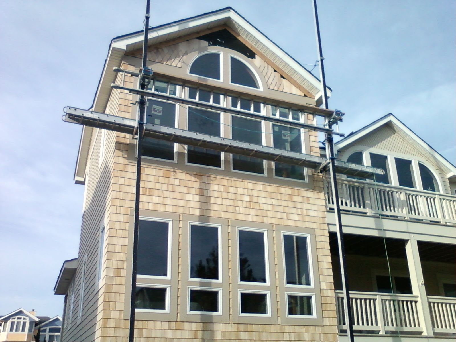 Two-story house with shingle siding, multiple windows, and scaffolding; blue sky.