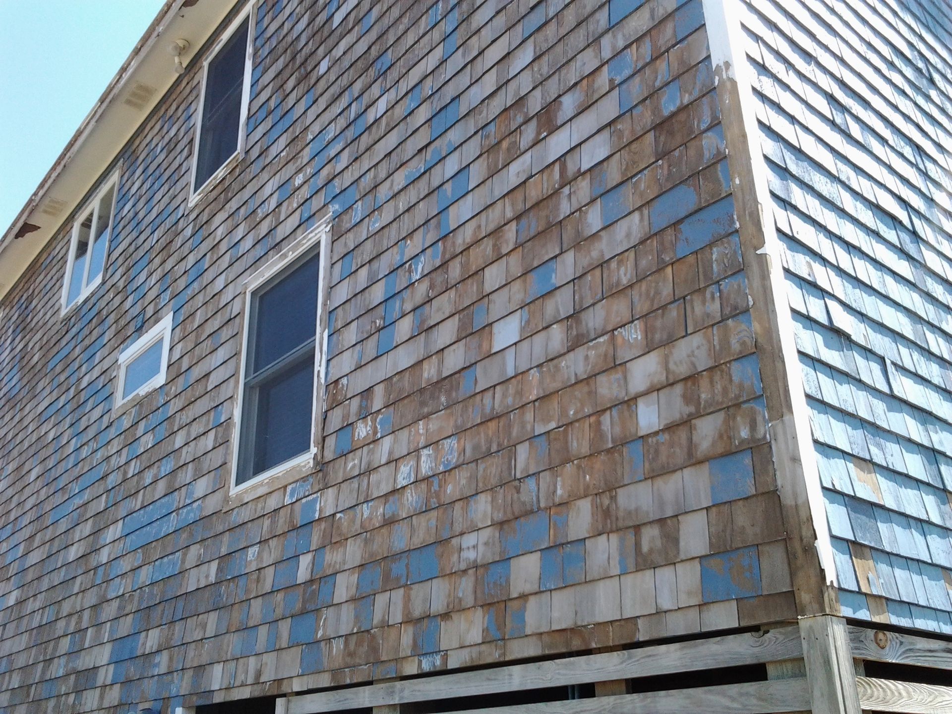 Weathered building exterior with blue paint on wooden shingles and several windows.