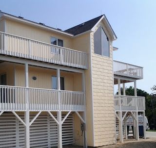 Two-story yellow beach house with white railings, balconies, and a tall, shingled accent.