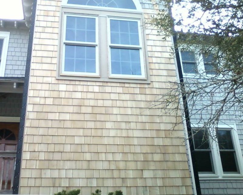 Exterior view of a building with cedar shingles, windows, and an arched window. A second building is on the right.
